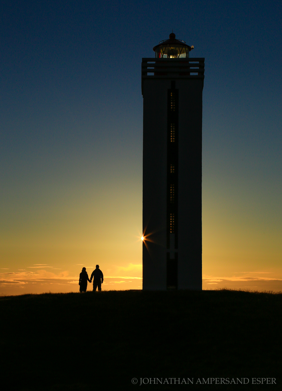 Couple walks around Kalfshamarsvik Lighthouse in northern Iceland at sunset